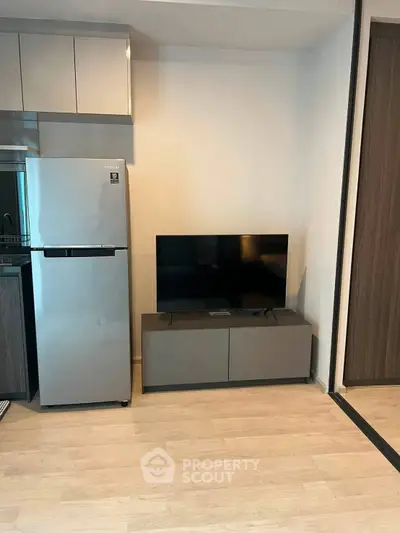 Modern apartment interior with sleek kitchen and stylish living area featuring a flat-screen TV and stainless steel fridge.