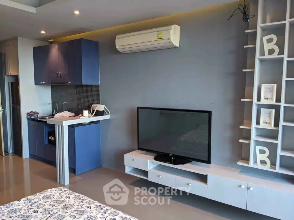 Modern studio apartment with sleek blue kitchen cabinets and wall-mounted TV.