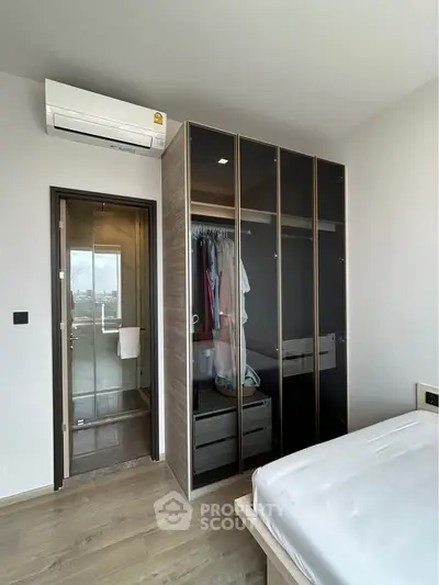 Modern bedroom with glass wardrobe and air conditioning, featuring a sleek design and natural light.