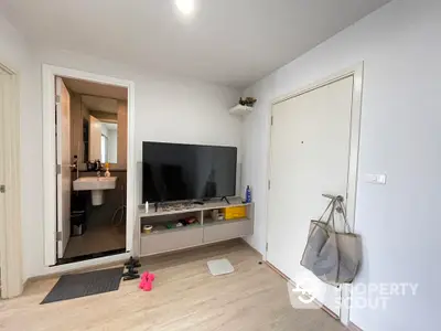 Spacious living room with modern flooring and ample natural light, featuring a large flat-screen TV and a convenient layout leading to an adjoining room.