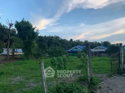 Scenic view of a lush green plot with surrounding houses and clear blue sky, ideal for residential development.