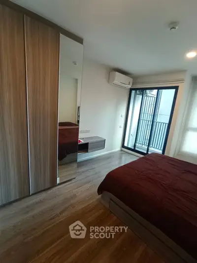 Modern bedroom with wooden flooring, mirrored wardrobe, and balcony access in a stylish apartment.