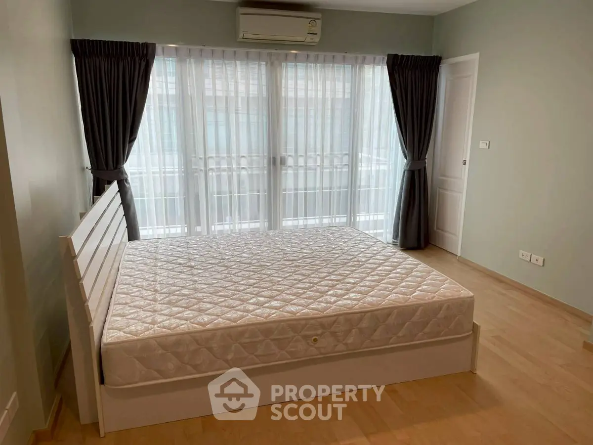Spacious bedroom with large windows and natural light, featuring a comfortable bed and elegant curtains.