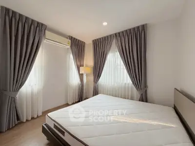 Spacious bedroom with large windows and elegant curtains, featuring a comfortable mattress and modern lighting.