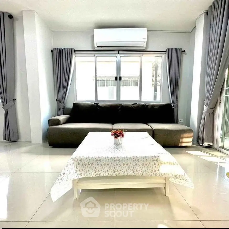 Spacious living room with modern sofa and air conditioning, featuring large windows and elegant curtains.