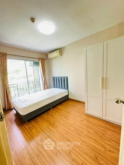 Bright bedroom with wooden flooring, large window, and modern furnishings in a cozy apartment.