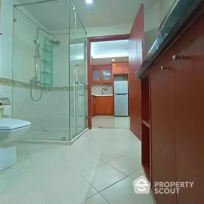 Spacious bathroom with glass shower and view into modern kitchen