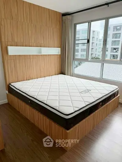 Modern bedroom with large window and wooden accents, featuring a comfortable mattress.