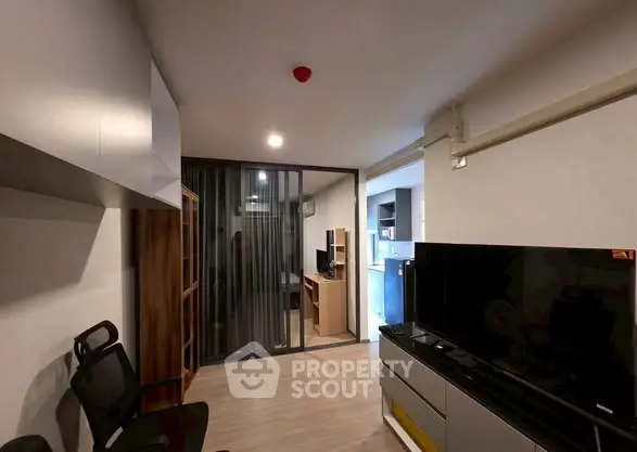 Modern living room with sleek TV setup and glass partition leading to study area.