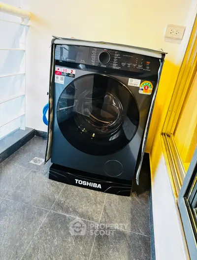 Modern Toshiba washing machine on a sleek balcony with glass railing.