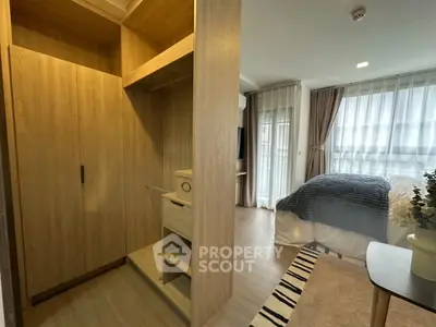 Modern bedroom with wooden closet and large windows, featuring cozy decor and natural light.