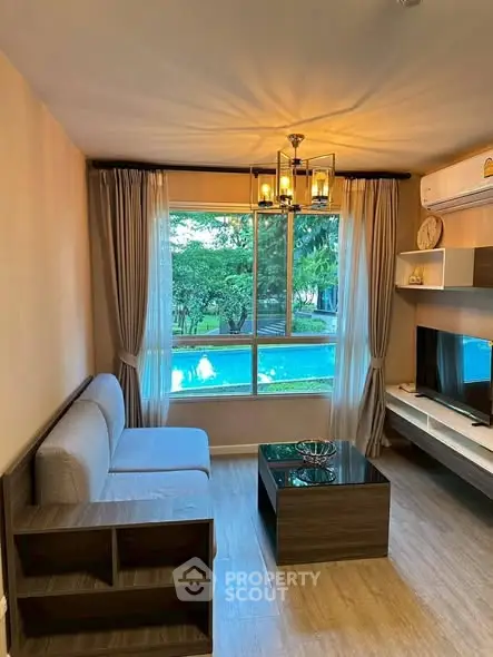 Modern living room with large window overlooking lush greenery and pool, featuring stylish furniture and elegant lighting.