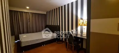 Stylish bedroom with striped walls and cozy lighting, featuring a comfortable bed and a functional desk area.