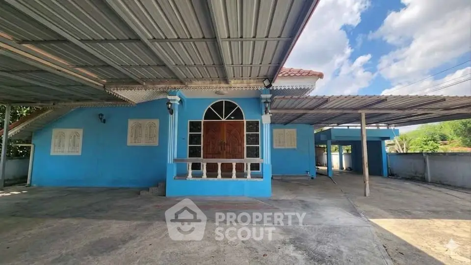 Charming blue house with spacious covered parking and inviting entrance under a clear sky.