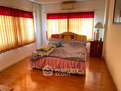 Cozy bedroom with wooden flooring and large windows, featuring a Garfield-themed bed and vibrant curtains.