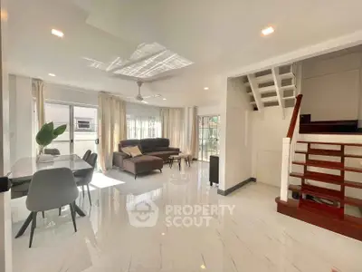 Spacious modern living room with elegant dining area and staircase, featuring abundant natural light.