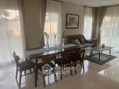 Elegant living room with modern dining set and cozy seating area, large windows offer garden view.