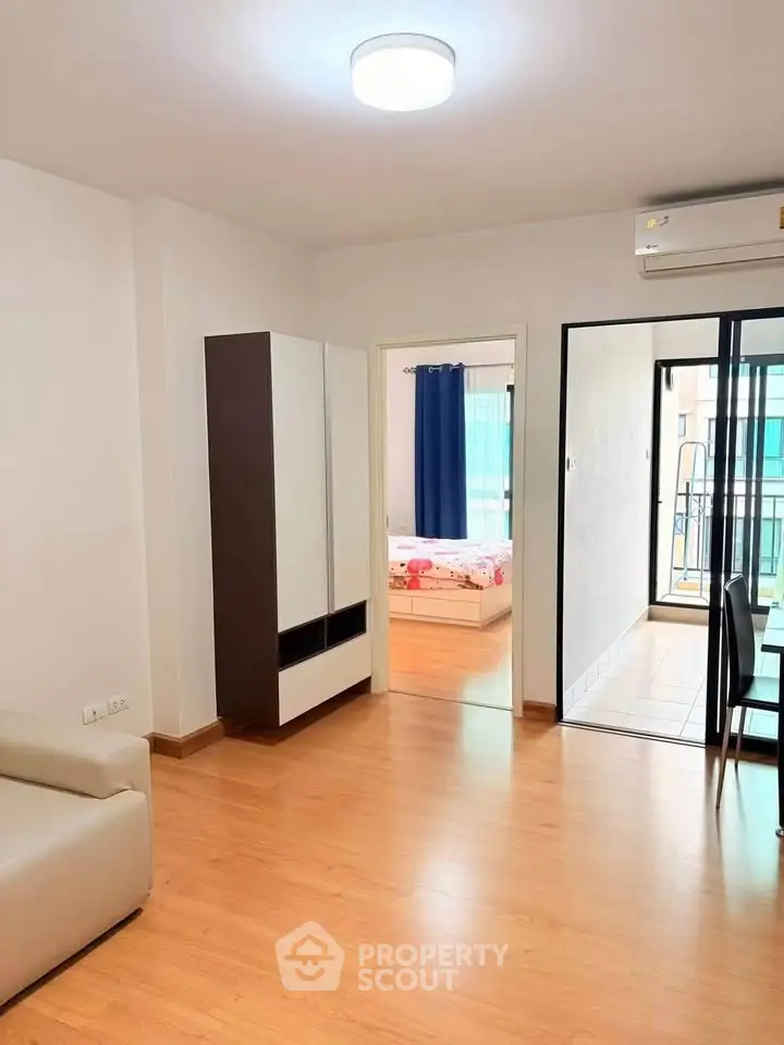 Modern apartment interior with wooden flooring, cozy living area, and a glimpse of the bedroom and balcony.