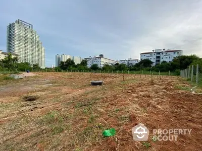 Expansive undeveloped land parcel available for sale, offering a blank canvas for a visionary developer, with urban skyline in the background.