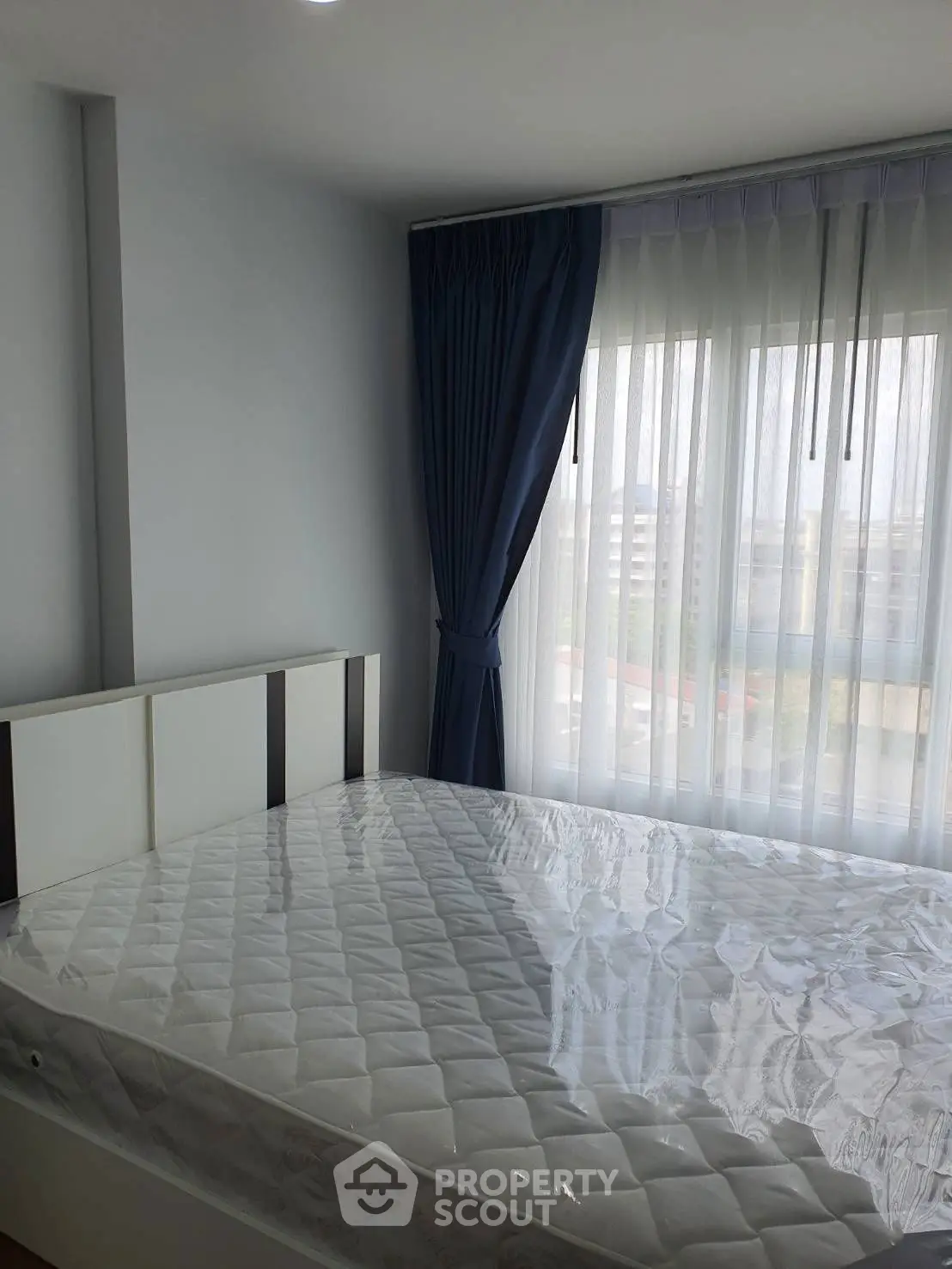 Bright bedroom with large window and modern decor, featuring a comfortable mattress and elegant curtains.