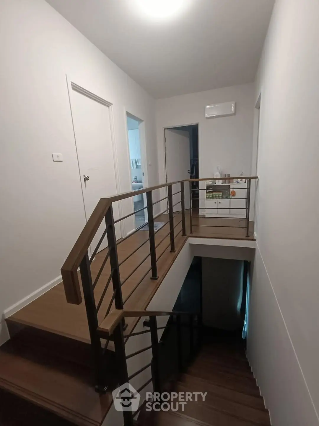 Modern staircase with wooden steps and metal railing in a well-lit hallway.