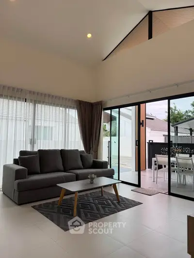 Spacious modern living room with high ceilings and large windows opening to a patio, perfect for entertaining.