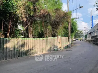 Urban street view with concrete fence and lush greenery, ideal for development opportunities.