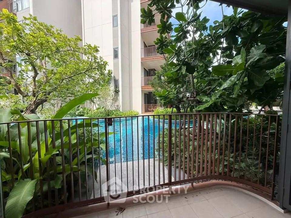 Charming balcony view overlooking lush greenery and a serene pool in a modern residential complex.