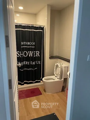Modern bathroom with stylish black shower curtain, pristine white toilet, and elegant red bath mat, offering a cozy and inviting atmosphere.