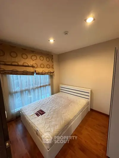 Cozy bedroom with wooden flooring and large window for natural light.