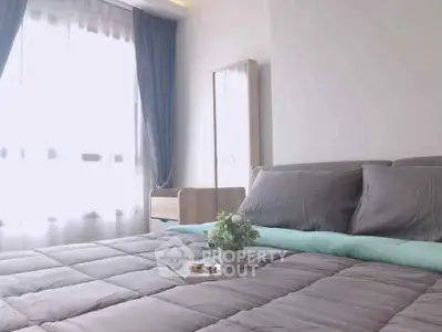 Cozy bedroom with soft gray bedding and natural light from large window.