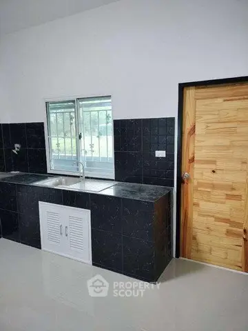 Modern kitchen with sleek black countertops and wooden door, featuring a window for natural light.