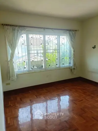 Bright empty room with polished wooden floors and large window view.
