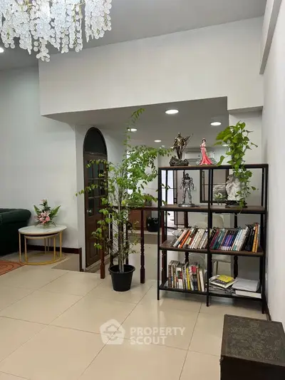Spacious living room with elegant decor and indoor plants, featuring a stylish bookshelf and chandelier.