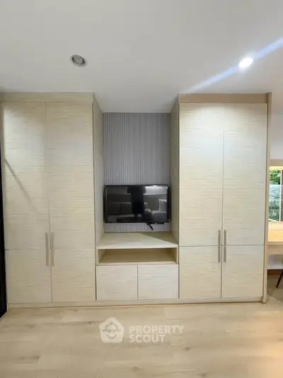 Modern living room with built-in storage and TV, featuring sleek design and ample natural light.
