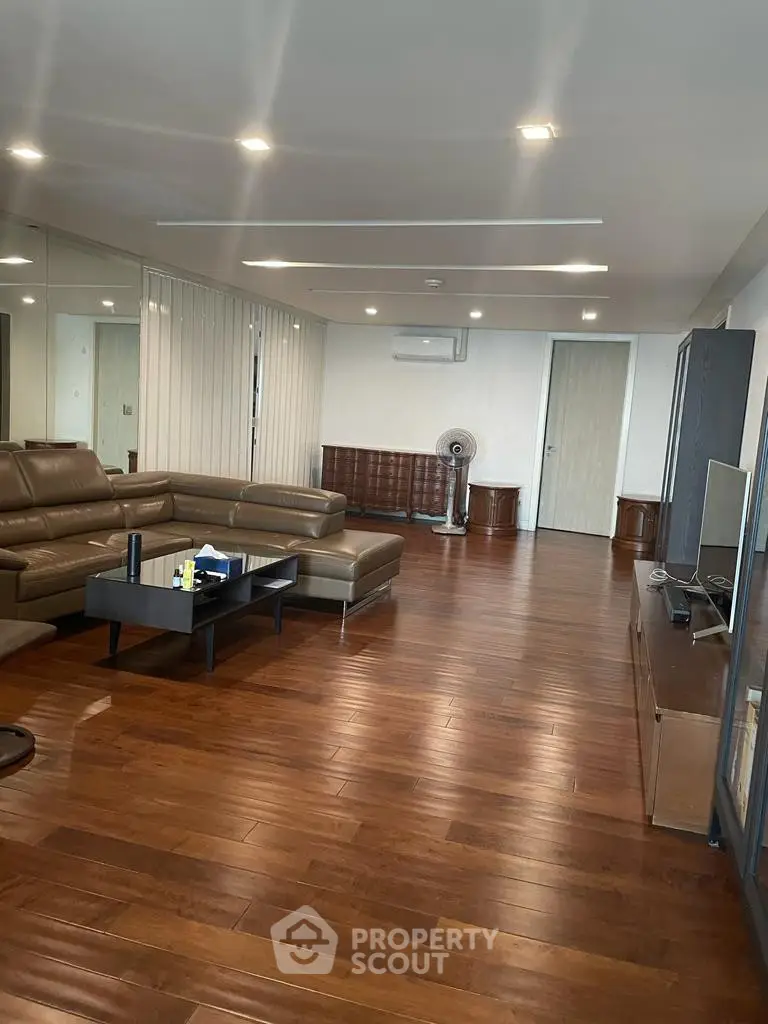 Spacious living room with elegant wooden flooring and modern leather furniture.