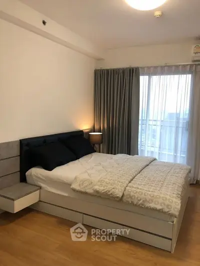 Modern bedroom with stylish decor and large window offering natural light and city view.