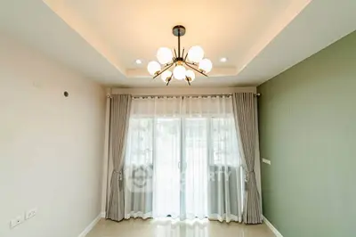 Elegant living room with modern chandelier and large window draped with curtains, offering ample natural light.