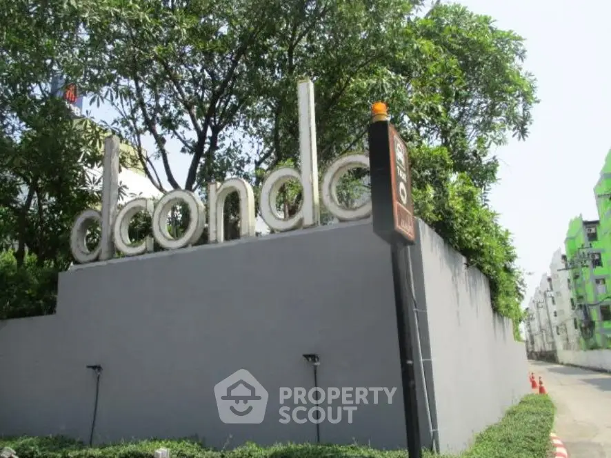 Modern condo entrance with lush greenery and sleek signage in urban setting.