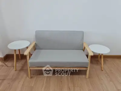 Minimalist living room with modern gray sofa and wooden side tables on hardwood floor.
