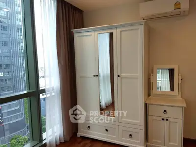 Modern bedroom with elegant wardrobe and vanity, featuring large window with city view.
