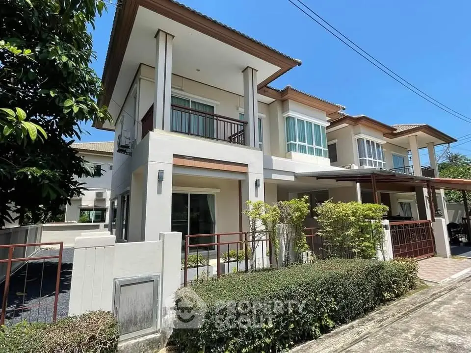 Modern two-story house with lush greenery and spacious balcony in a serene neighborhood.