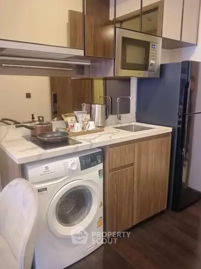 Compact modern kitchen with washing machine, microwave, and sleek cabinetry.