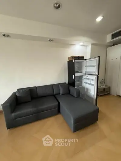 Modern living room with sleek black sofa and open fridge, showcasing minimalist design and functionality.