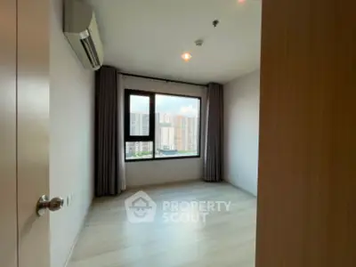 Spacious bedroom with large window offering city view in modern apartment.