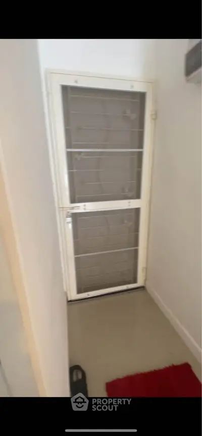 Small entryway with security door and red rug in a residential property.