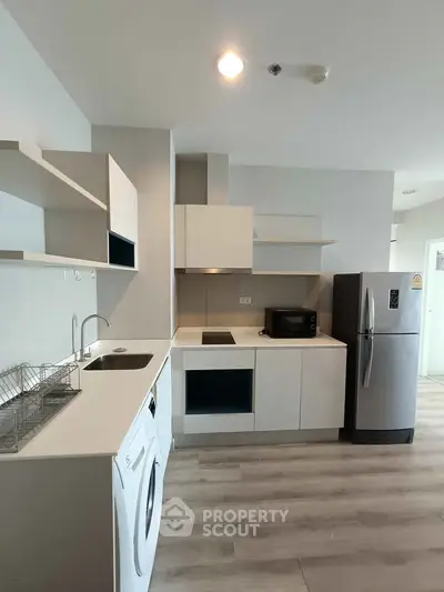 Modern kitchen with sleek appliances and open layout, featuring washing machine and fridge.