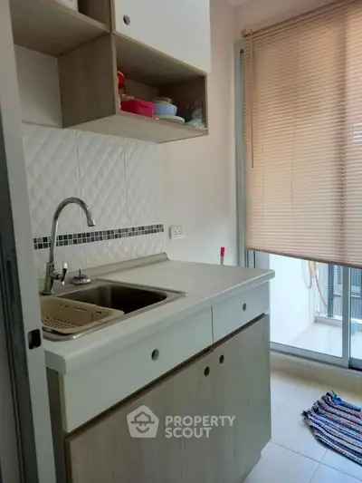 Compact kitchen with modern sink and ample natural light from large window.