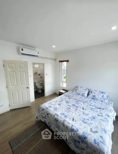 Bright bedroom with floral bedding and ensuite bathroom, featuring modern air conditioning and natural light.