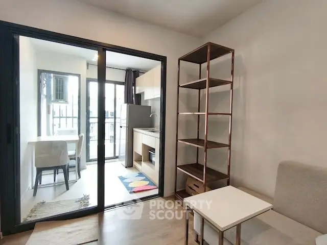 Modern living room with open kitchen and balcony access, featuring sleek shelving and cozy seating.